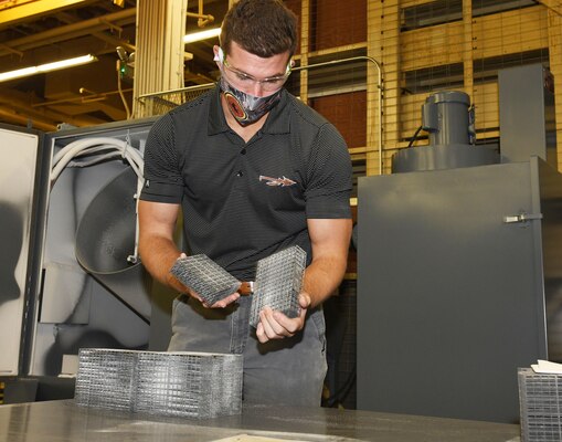 Fleet Readiness Center Southeast (FRCSE) mechanical engineer, Evan Grambling, removes 3D printed nasopharyngeal swab cages from the automated glass bead blaster after a timed blasting cycle.