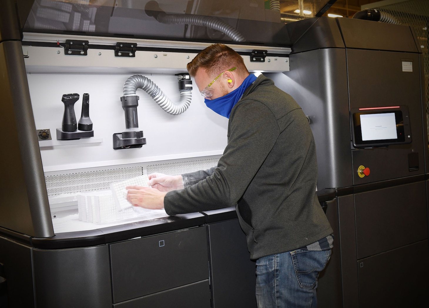 Fleet Readiness Center Southeast (FRCSE) mechanical engineer, Matthew Simon, removes excess nylon powder from 3D printed nasopharyngeal swab cages before going into an automated glass bead blaster for further processing.