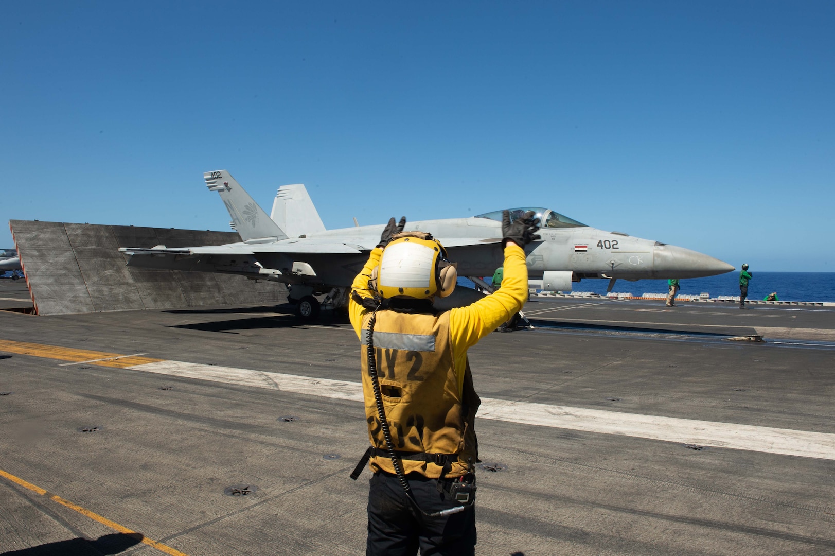A service member directs a jet taking off from an aircraft carrier.