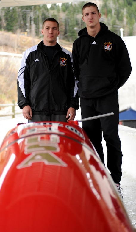Two men stand beside a bobsled.