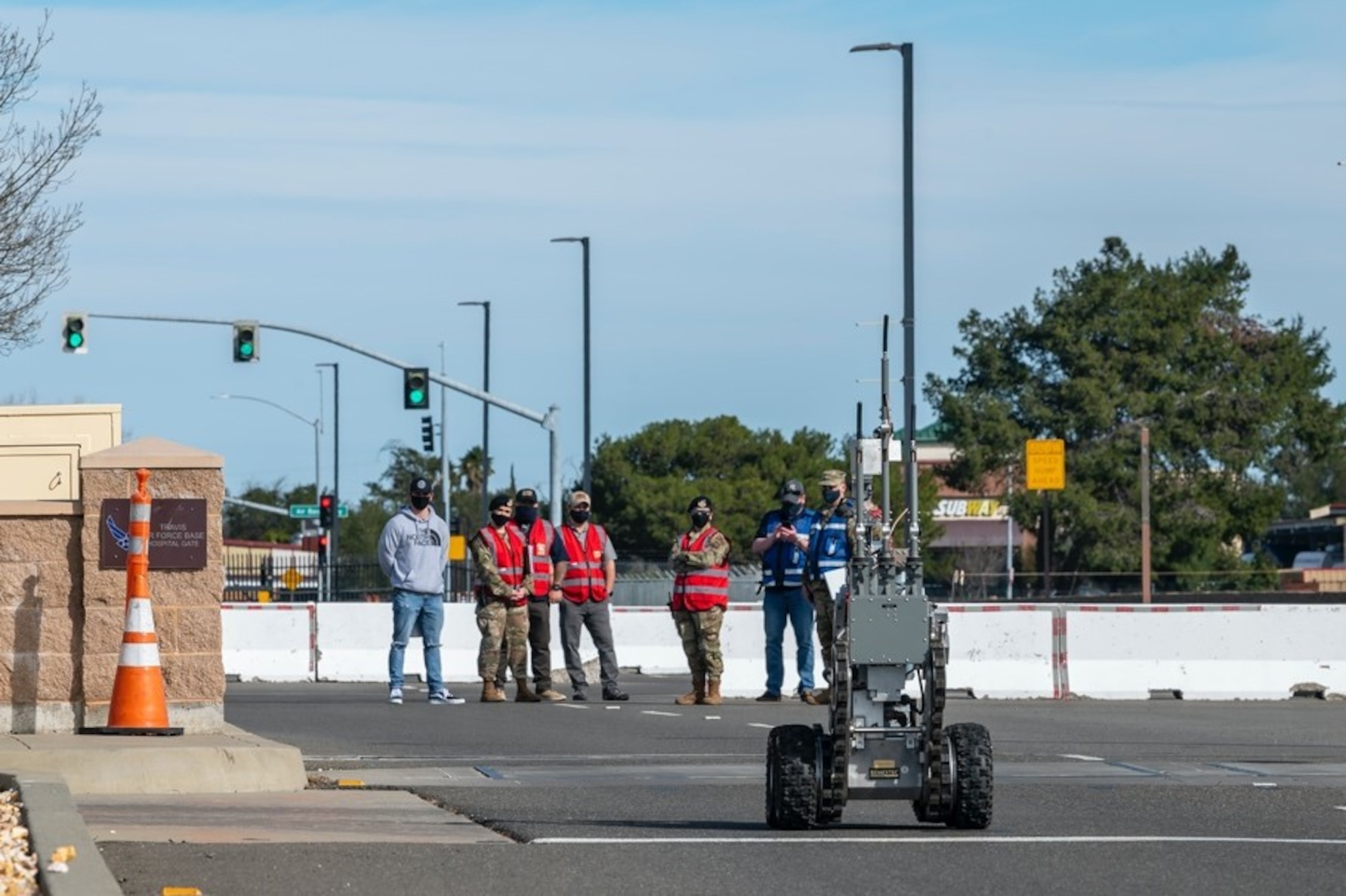 Airmen in bright vests look on at a bomb disposal robot