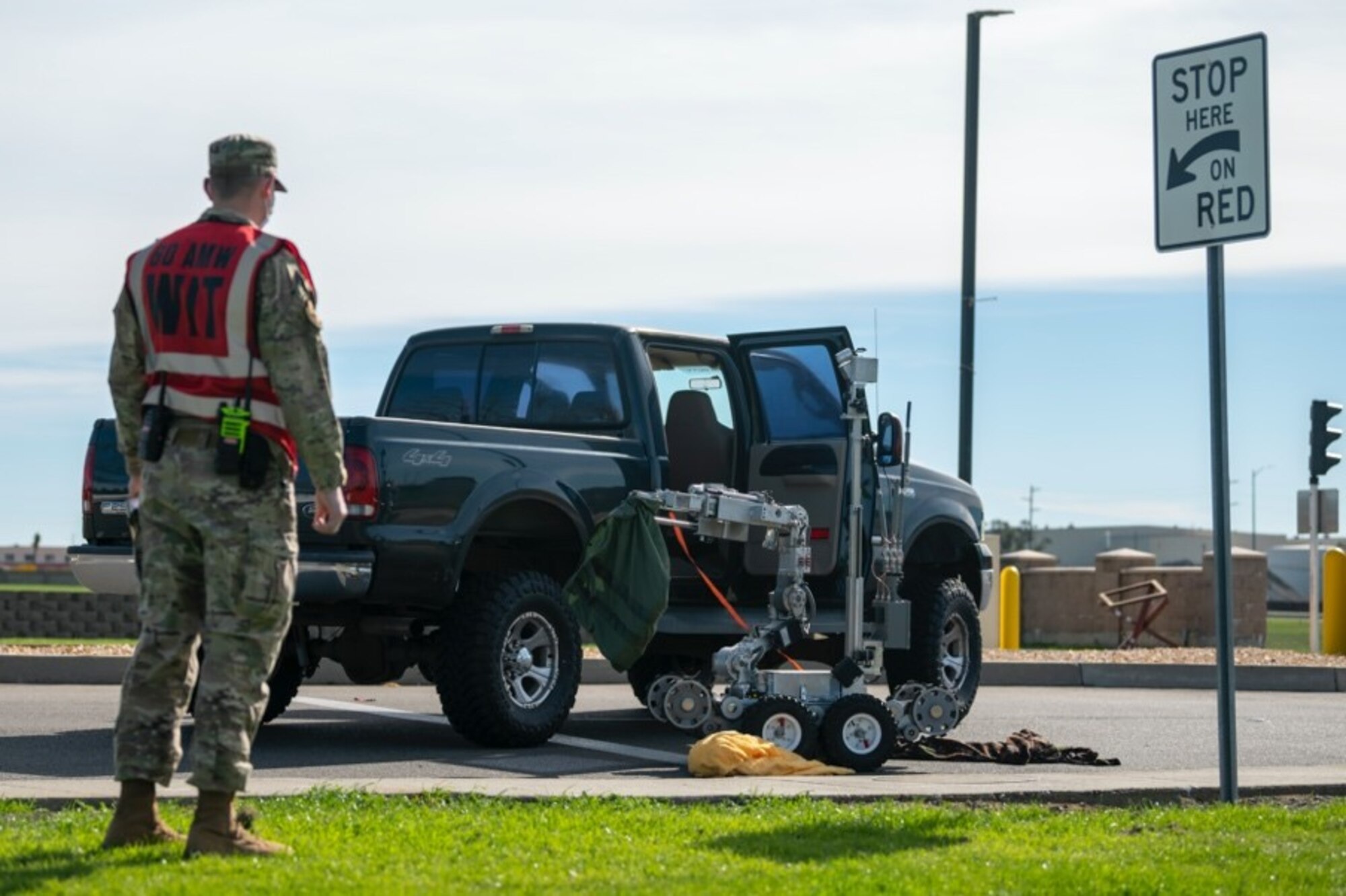An Airman in a bright vest looks on at a parked truck with the door open