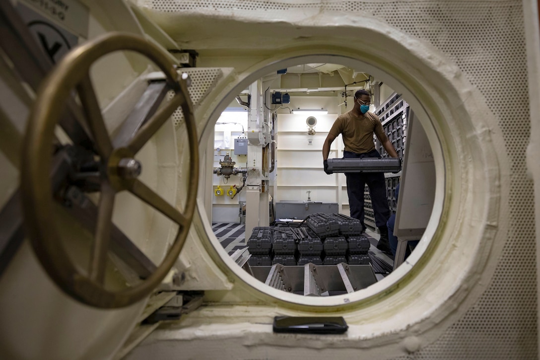 A sailor stores ammo on a ship as seen through the open door of a vault.