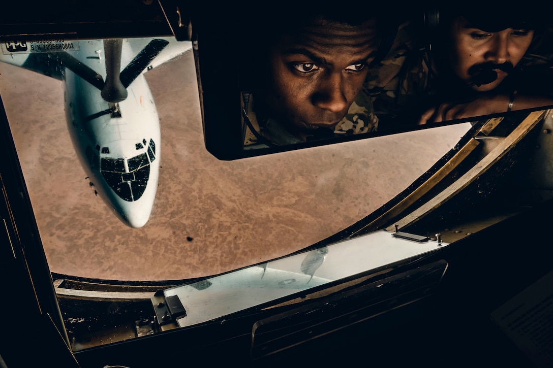 Airmen watch an aircraft refuel as seen through a mirror.