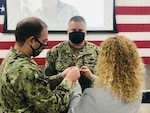 Megan Atkinson pins a rank insignia Dec. 12, 2020, on Petty Officer 2nd Class Trevor Atkinson of Winter Haven, Florida, during a virtual meritorious advancement ceremony at Coast Guard Port Security Unit 307 in Clearwater, Florida. Atkinson, is a tactical boat crewman at PSU 307 and became the second Coast Guard reservist to be meritoriously advanced under a new program established by the commandant in March 2020. Coast Guard photo courtesy of Lt. Glenn Sanchez