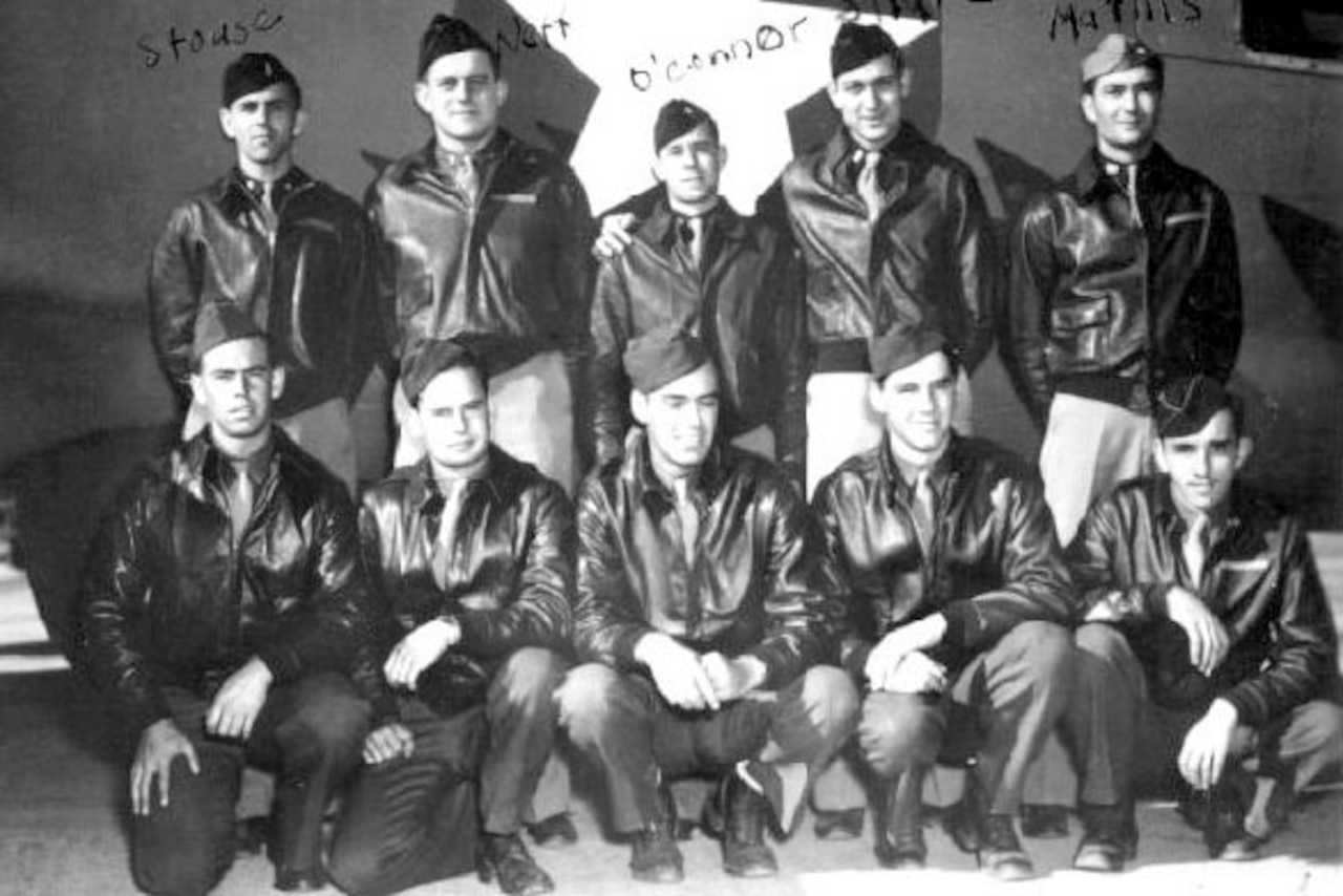 Five airmen kneel while another five stand for a photo in front of an airplane.