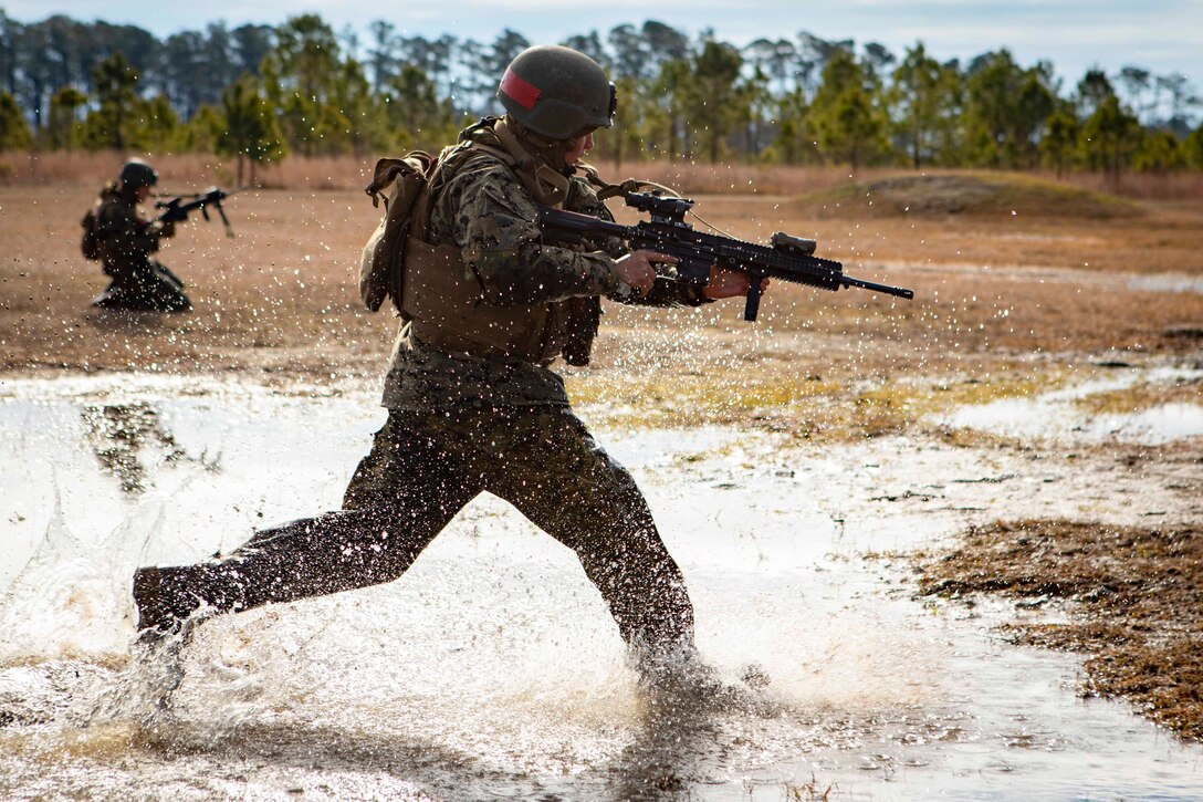A Marine runs through a puddle of water while holding a weapon.