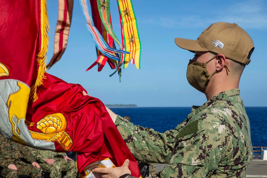 A sailor wearing a face mask holds a red flag.