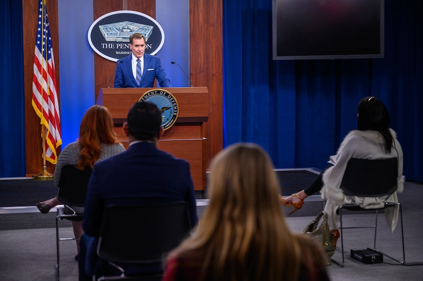 A man stands behind a lectern. In front of him are several
individuals seated in chairs.