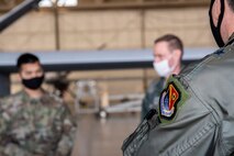 U.S. Air Force Warfare Center patch is displayed on the unit's vice wing commander's left arm as maintenance Airmen are briefing in the background, which is blurred.