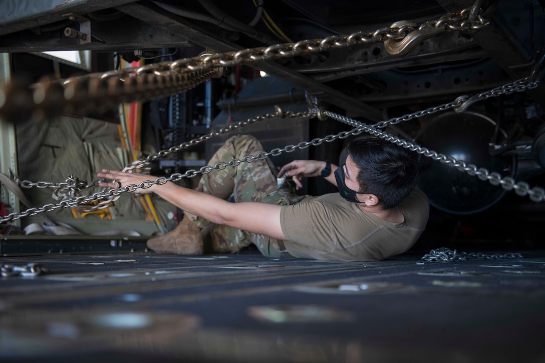 An airmen lays on the ground to secure a truck onto an aircraft.