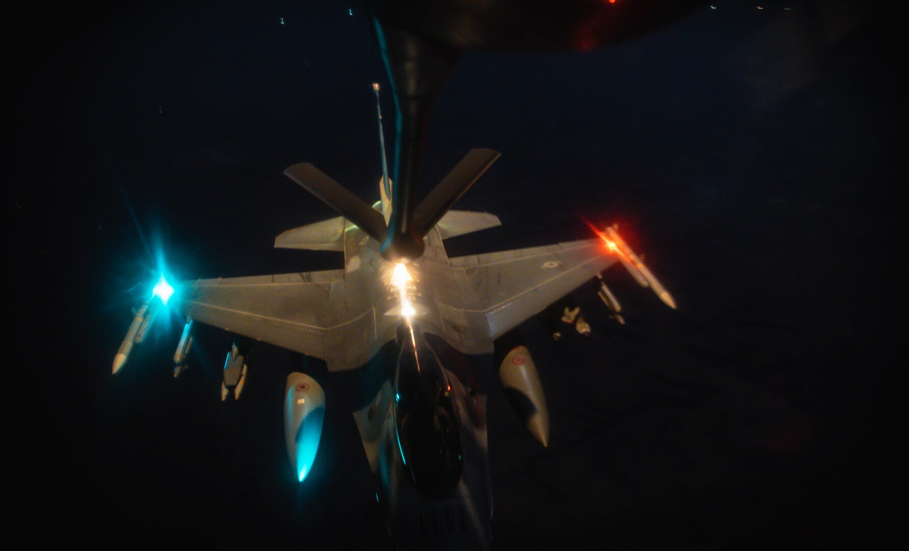 An airborne aircraft with red and blue lights receives fuel at night.