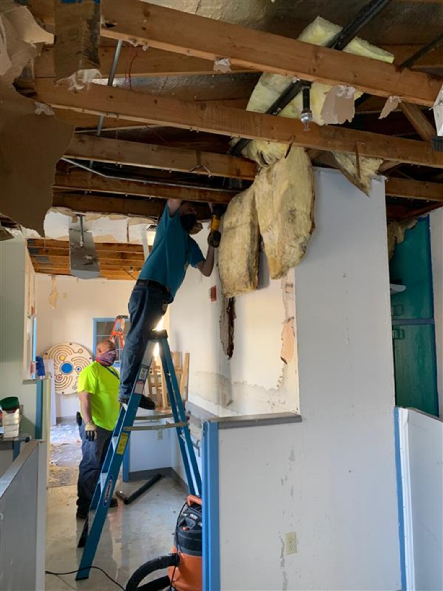 One male civilian stands on a ladder while repairing roof damage.