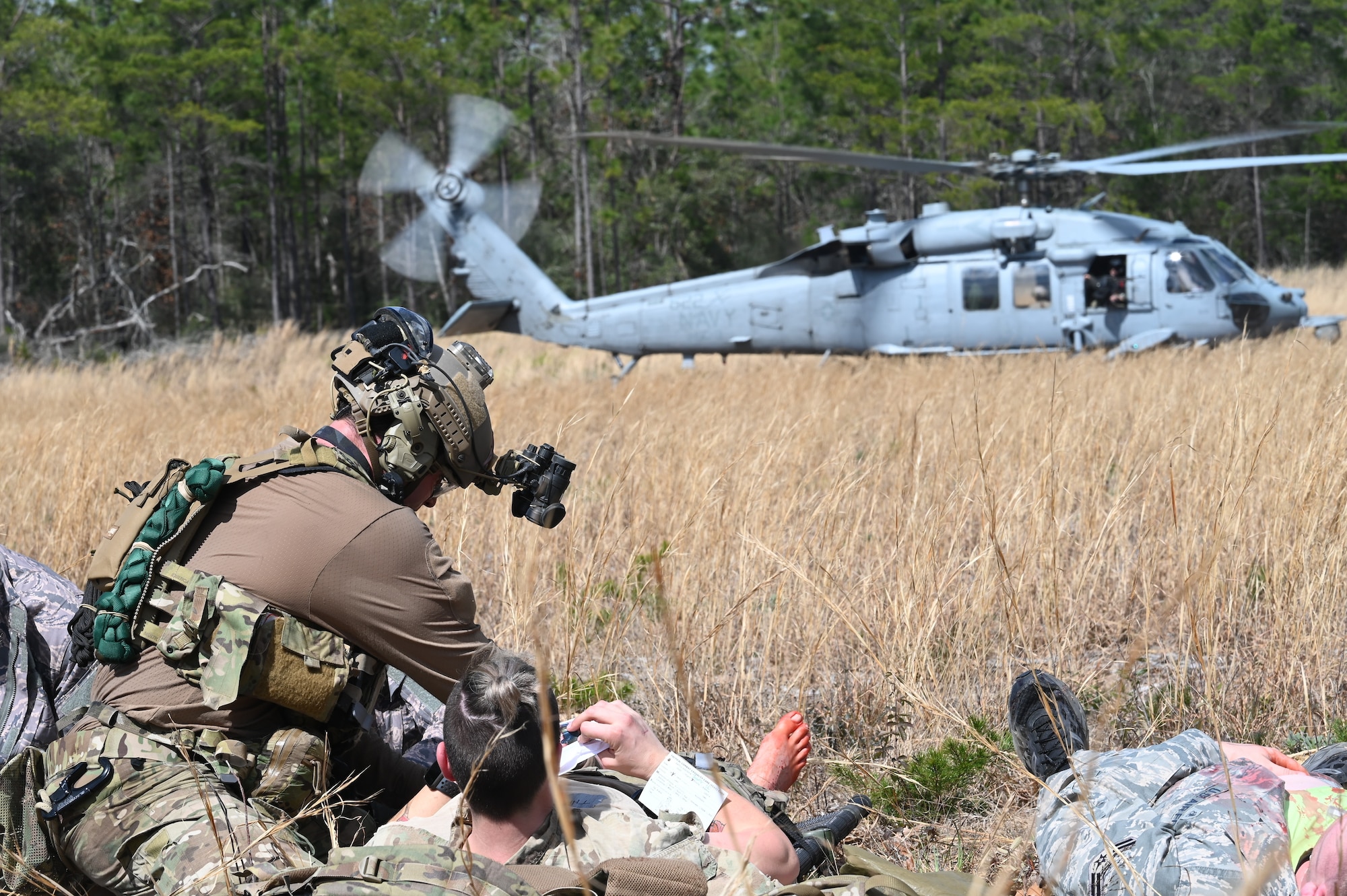 A U.S. Air Force Special Tactics operator assigned to the 24th Special Operations Wing provides medical care to a simulated casualty as a U.S. Navy MH-60 Sea Hawk from Helicopter Sea Combat Squadron Nine prepares to move casualties to a follow on medical treatment center during a personnel recovery training mission for Emerald Warrior 21.1, Feb. 25, 2021, at the Eglin Range Complex, Florida. Emerald Warrior is the largest joint special operations exercise involving U.S. Special Operations Command forces training to respond to various threats across the spectrum of conflict. (U.S. Air Force photo by Master Sgt. Jason Robertson/Released)