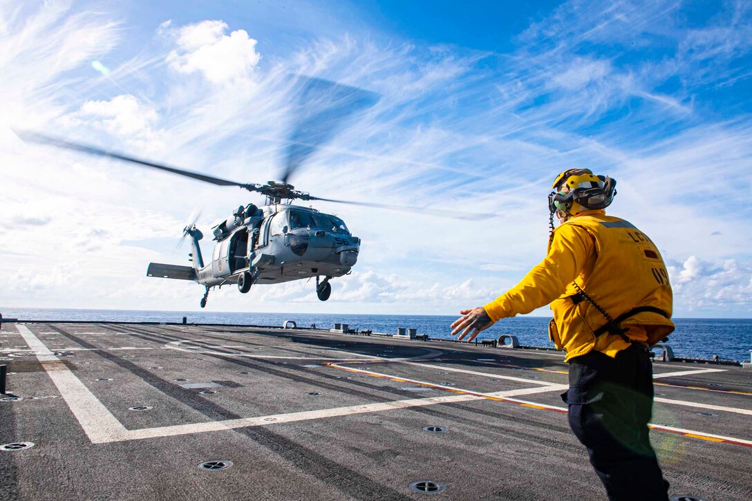 A sailor signals to a helicopter on the deck of a ship.