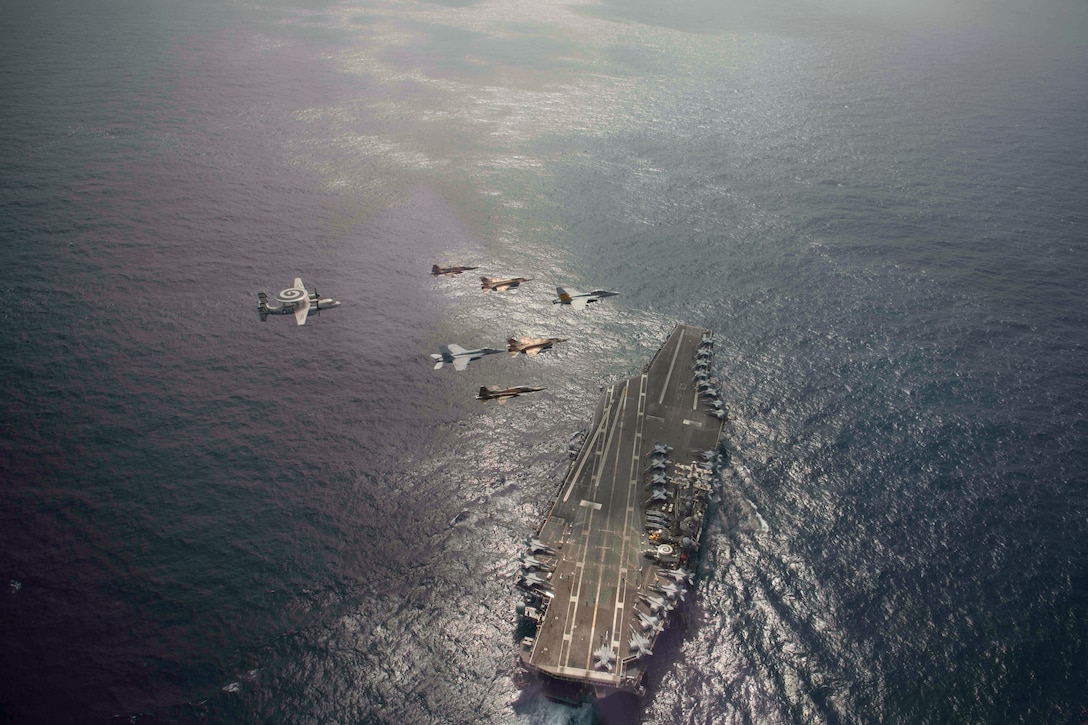 Aircraft fly in formation over a ship at sea.