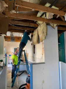 One male civilian stands on a ladder while repairing roof damage.