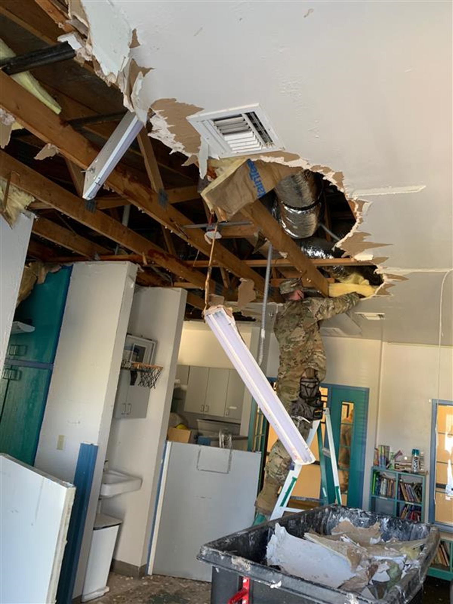 One male civilian stands on a ladder while repairing roof damage.