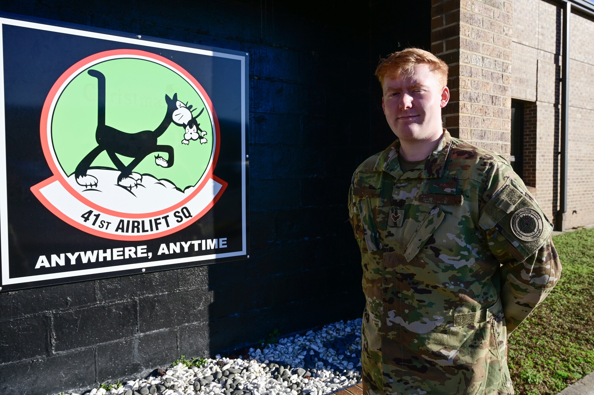 An Airman poses for a photo in front of a squadron sign.