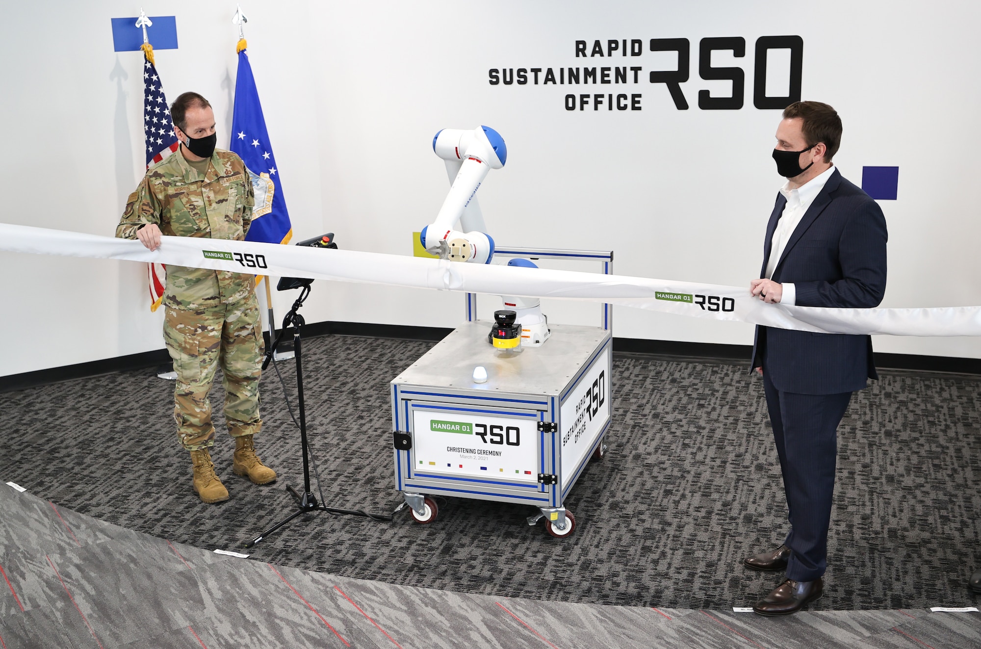 Lt. Gen. Shaun Morris, Air Force Life Cycle Management Center Commander (left) and Nathan Parker, RSO Deputy Program Executive Officer, with the help of a robotic arm, cut the ribbon on Hangar01, a new RSO workspace in Dayton, Ohio on March 2, 2021. (U.S. Air Force photo by Casey Tromp).