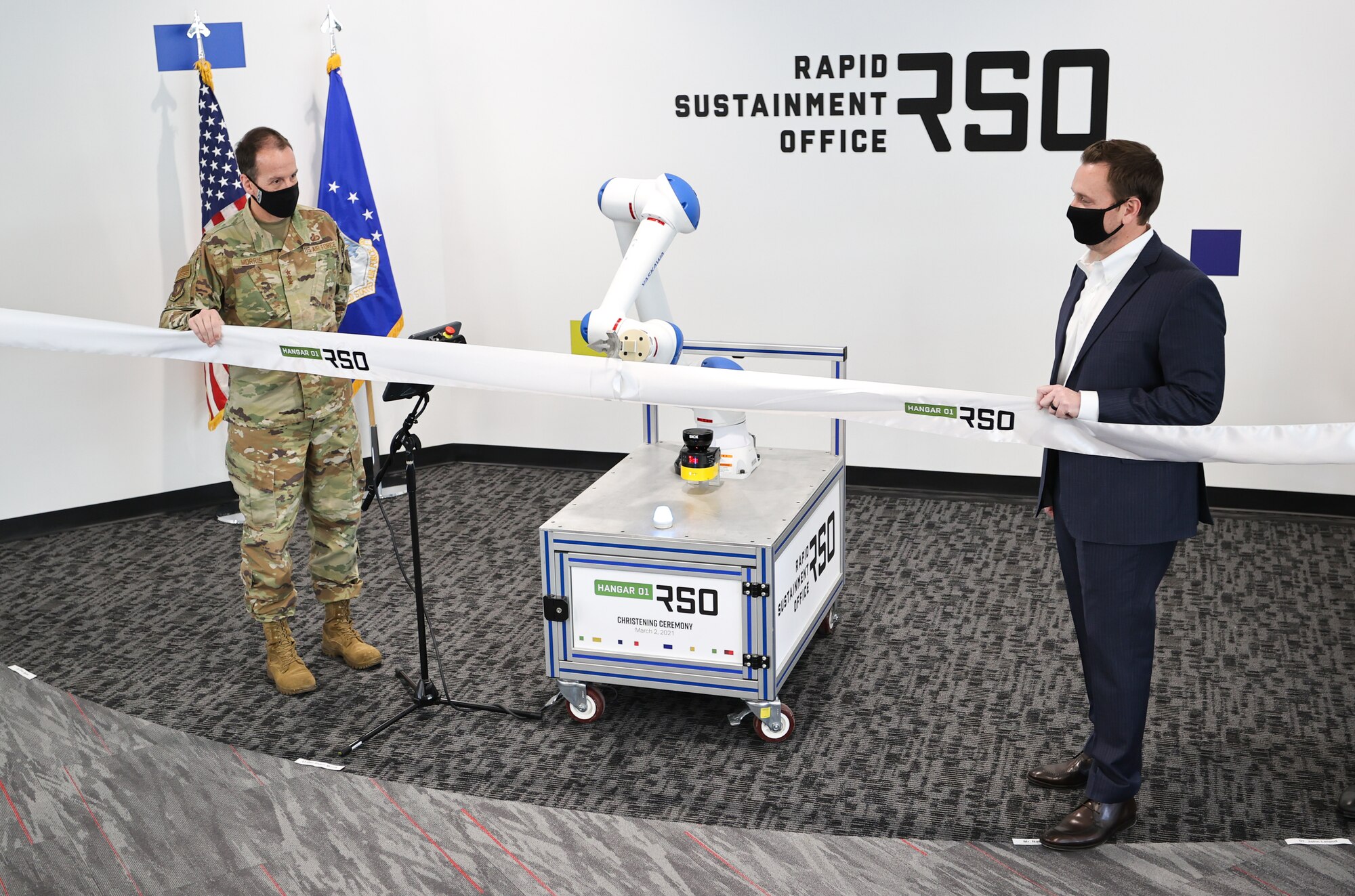 Lt. Gen. Shaun Morris, Air Force Life Cycle Management Center Commander (left) and Nathan Parker, RSO Deputy Program Executive Officer, with the help of a robotic arm, cut the ribbon on Hangar01, a new RSO workspace in Dayton, Ohio on March 2, 2021.