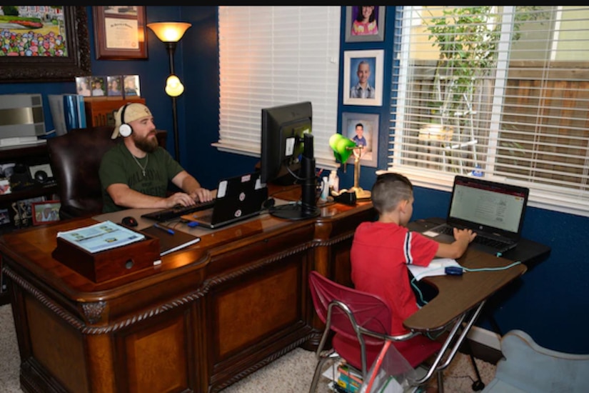 A father and son each sit at a desk in a shared home-office.