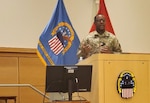 A man in operational camouflaged uniform speaks from behind a podium.