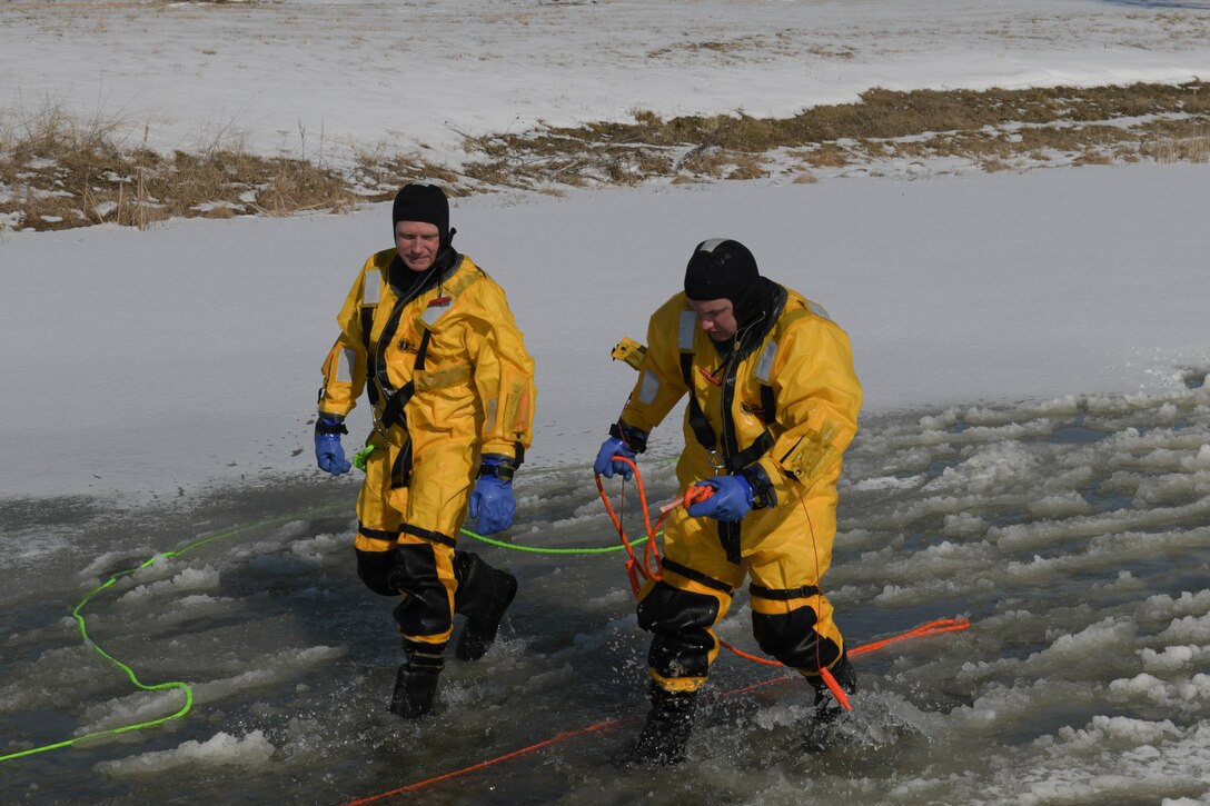 Two members of the Whiteman Air Force Base Fire department walk through shallow water and ice during cold water rescue training.