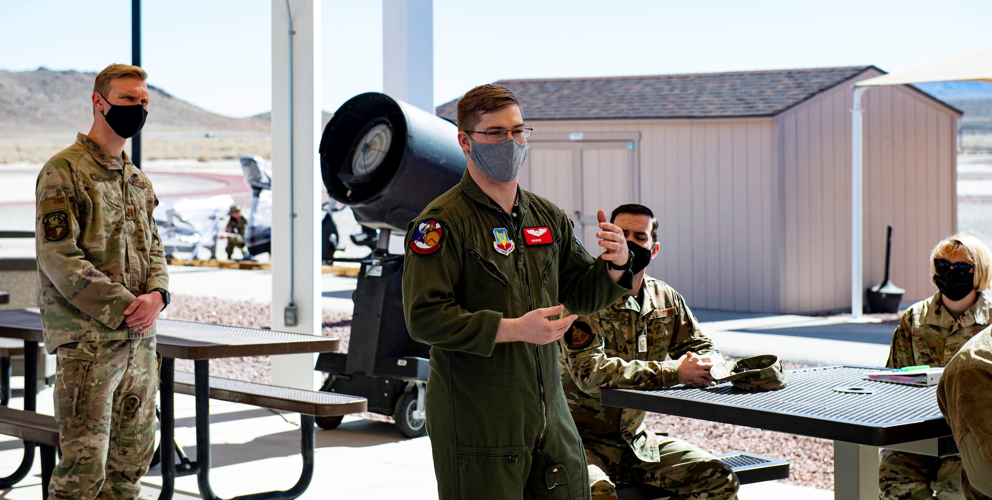 Male lieutenant speaks to a group of military members standing outside near picnic tables.