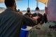 Male Colonel hands out sandwich to military members standing in line in an outdoor park bench seating area.