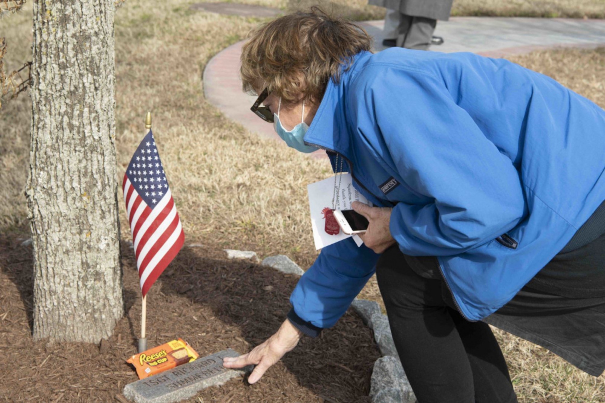 A woman touches a plaque in the ground under a tree