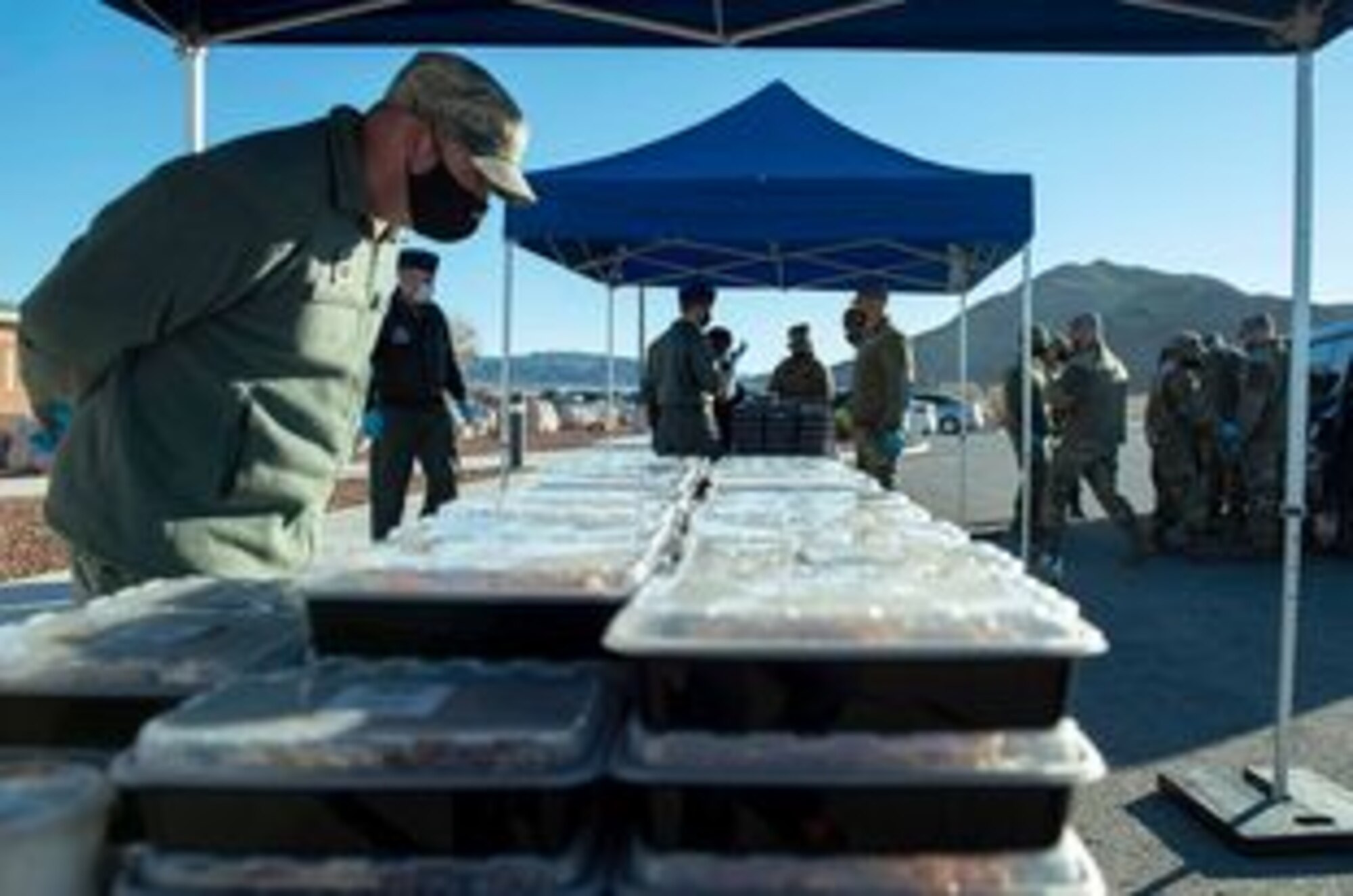 A male military member looks over stacks and rows of box meals in preparation for distribution.