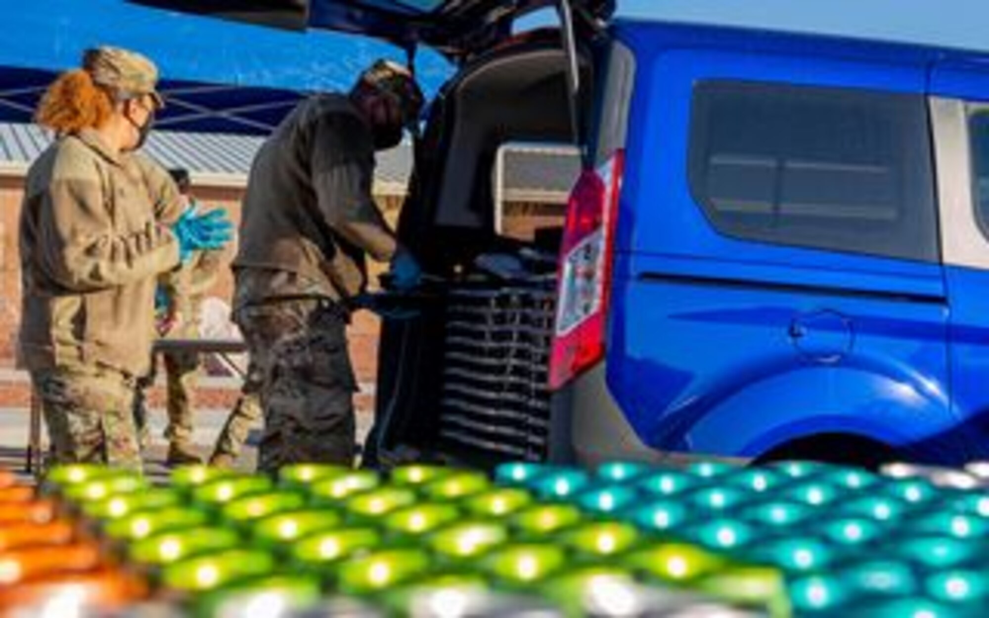 two military members collect stacks of box meals from the back of a vehicle.