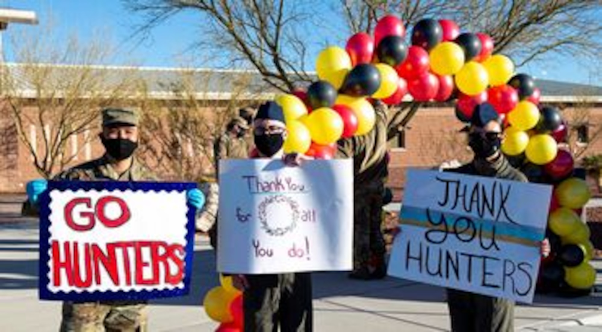 three military members hold different and colorful signs that read, "Thank you," "Thank you for all you do," and "Thank you Hunters."