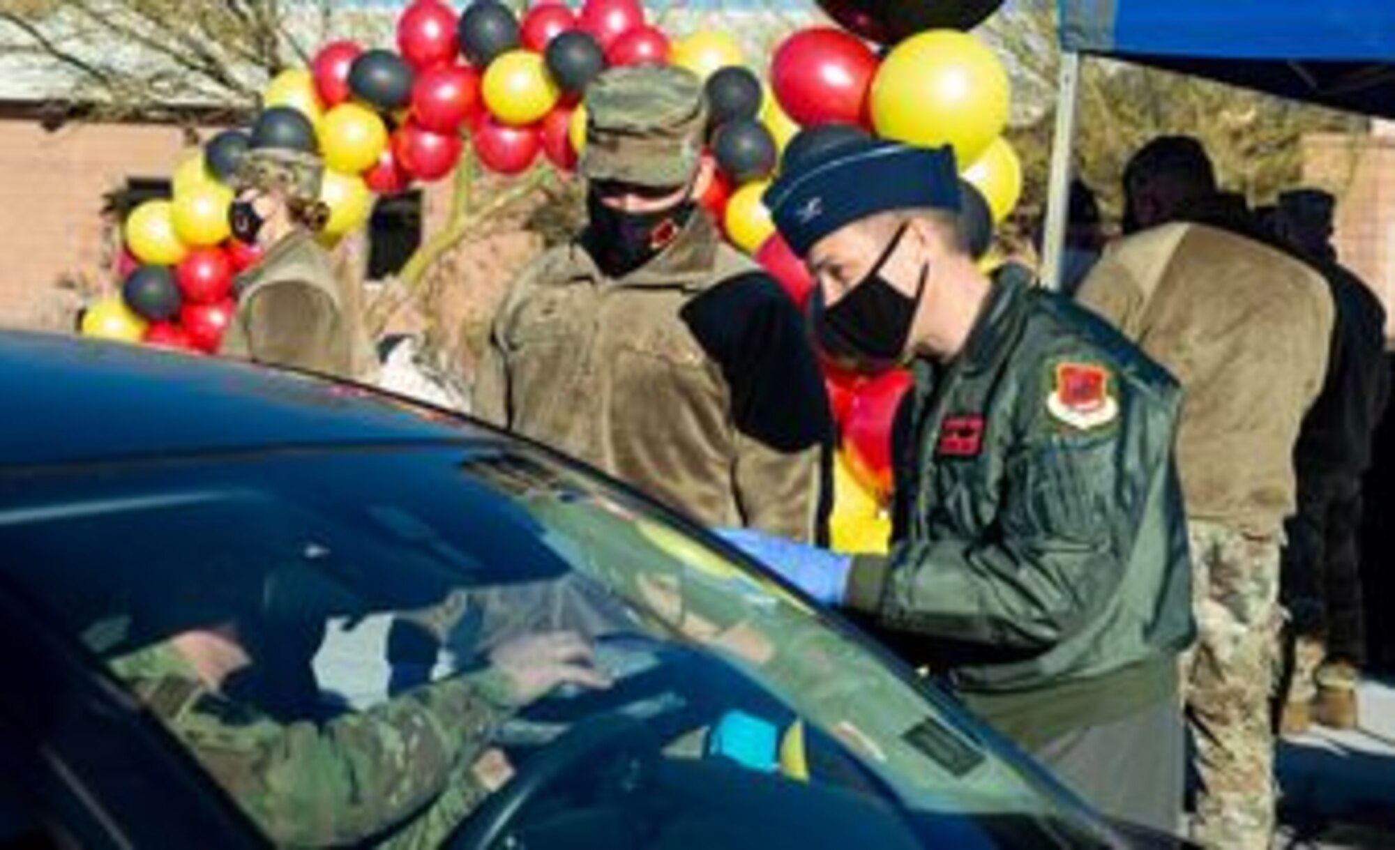 Male Colonel and Chief Master Sergeant stand in front of the drivers door to hand boxed meals to a military member in their car.