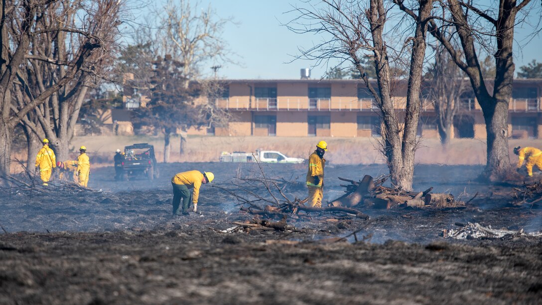 Tinker Firefighters picking up debris in a recently-burned field.