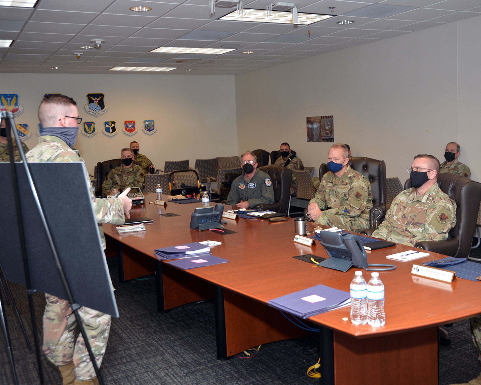 An officer in uniform briefs leadership in uniform around a table.