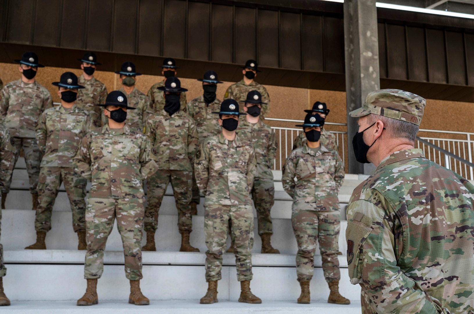 Military Training Instructors stand on bleachers in front of general in uniform.