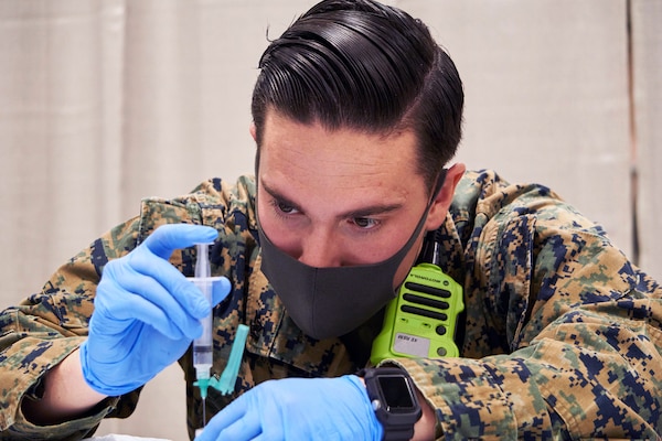 A sailor wearing a face mask and gloves holds a syringe  while preparing a COVID-19 vaccine.