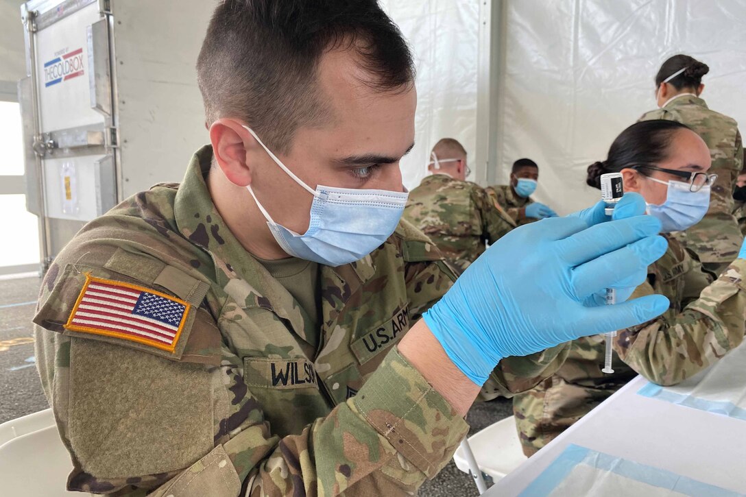 A man in a military uniform fills a syringe with a vaccine.