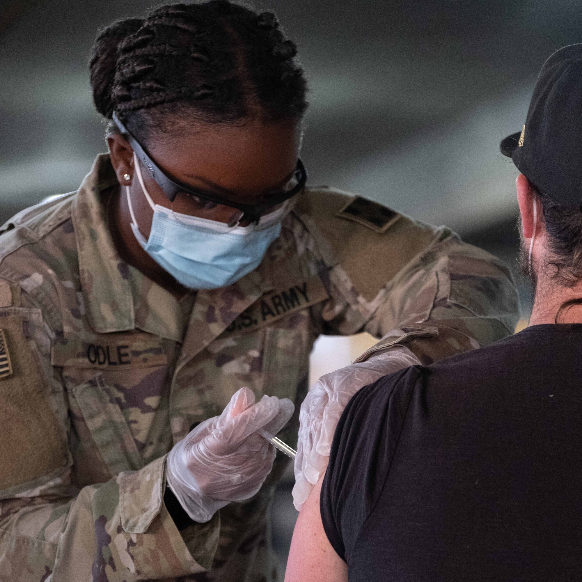 A woman in a military uniform injects a vaccine into the arm of a civilian.