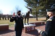 Male soldier in dress uniform raises right hand across from male soldier in dress uniform holding notebook.