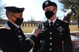 Male soldier in dress uniform pins branch insignia on male soldier in dress uniform.