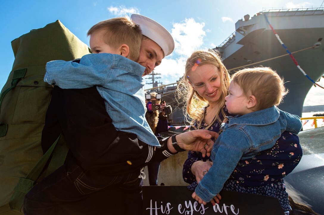 A sailor greets his family on a pier.