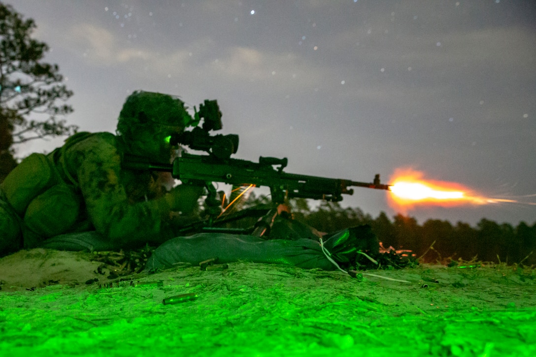 A Marine fires his machine gun at night under a green light.