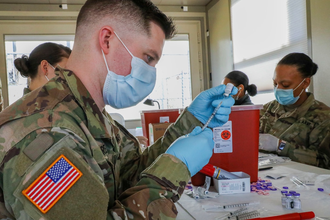 Four soldiers wearing face masks and gloves prepare syringes for COVID-19 vaccines.