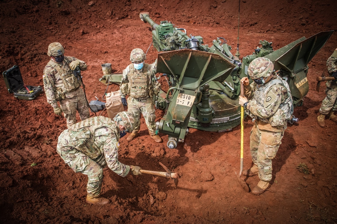 Four soldiers stand around a large gun and dig a hole in the ground.
