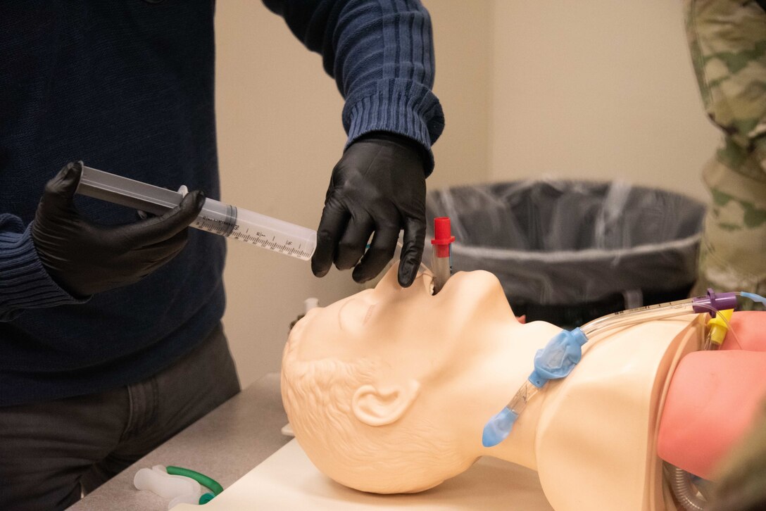 A person inserts a medical device through the nostril of a simulation dummy.