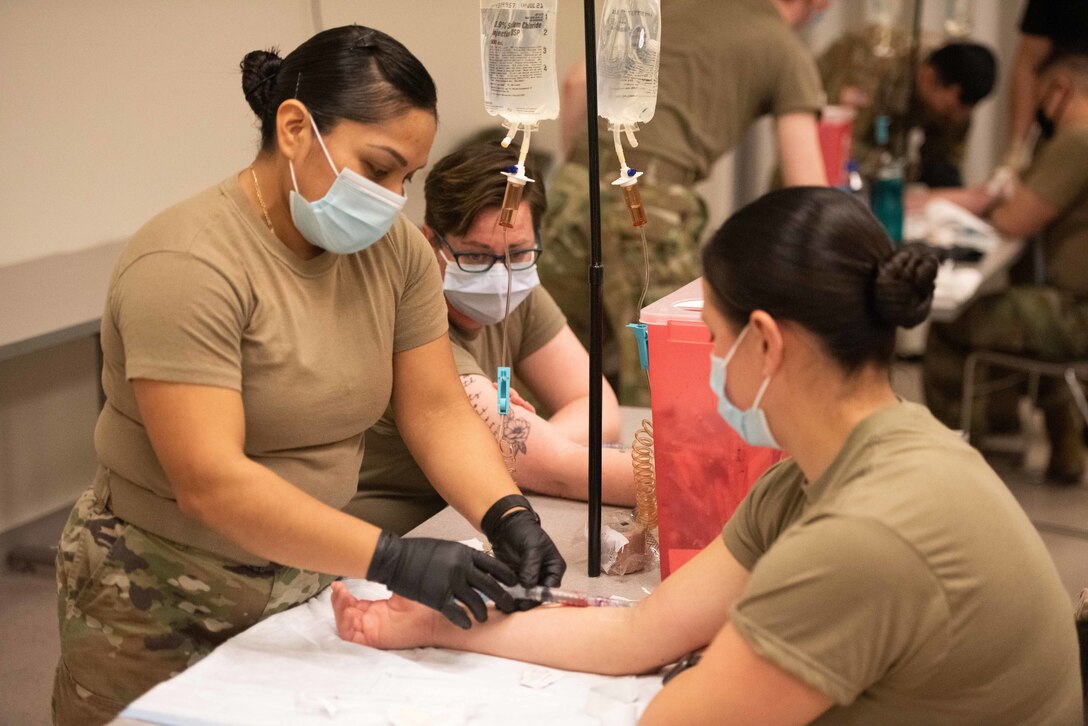 Three female soldiers practice a medical simulation.