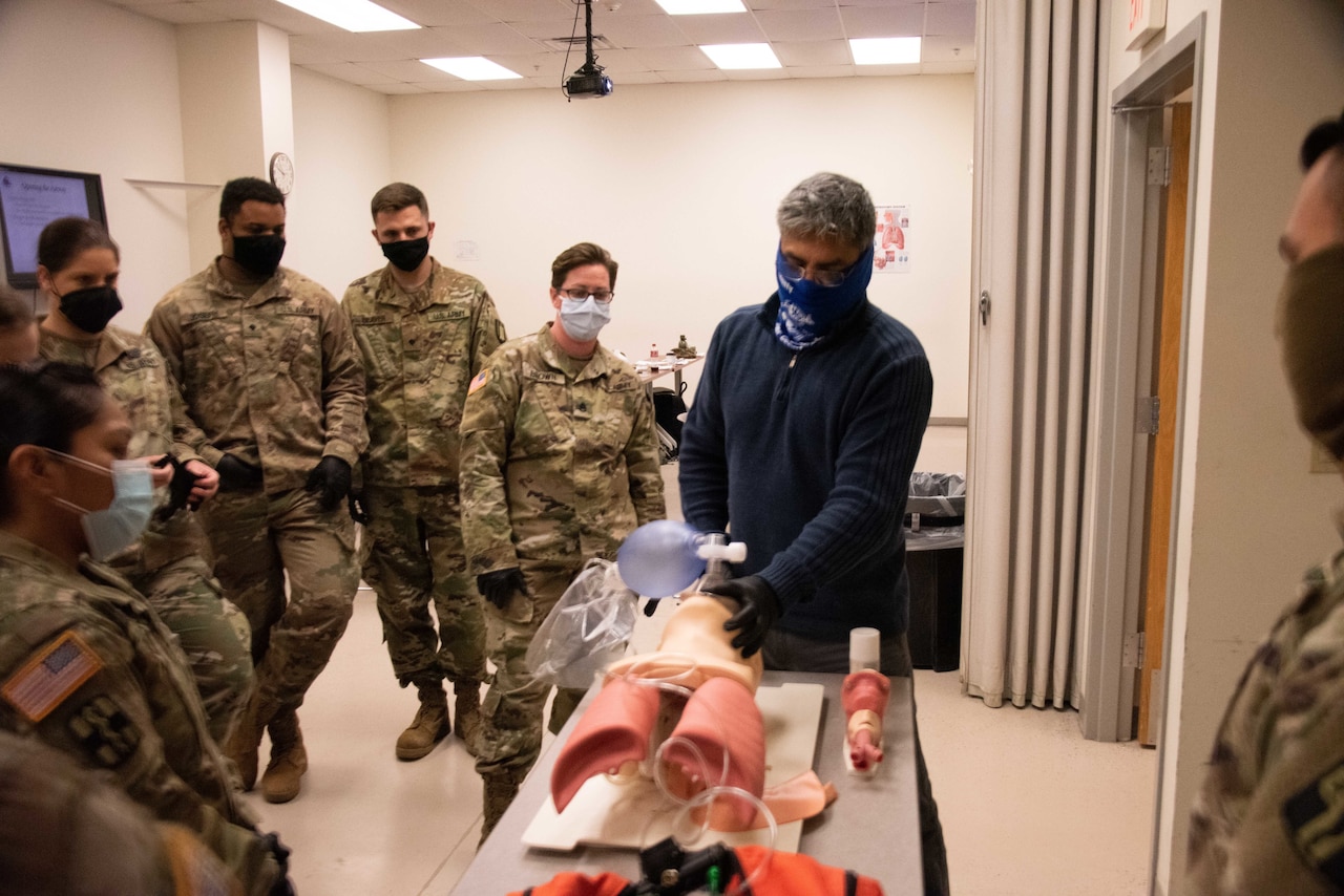 Soldiers watch an instructor interact with a medical simulation dummy.